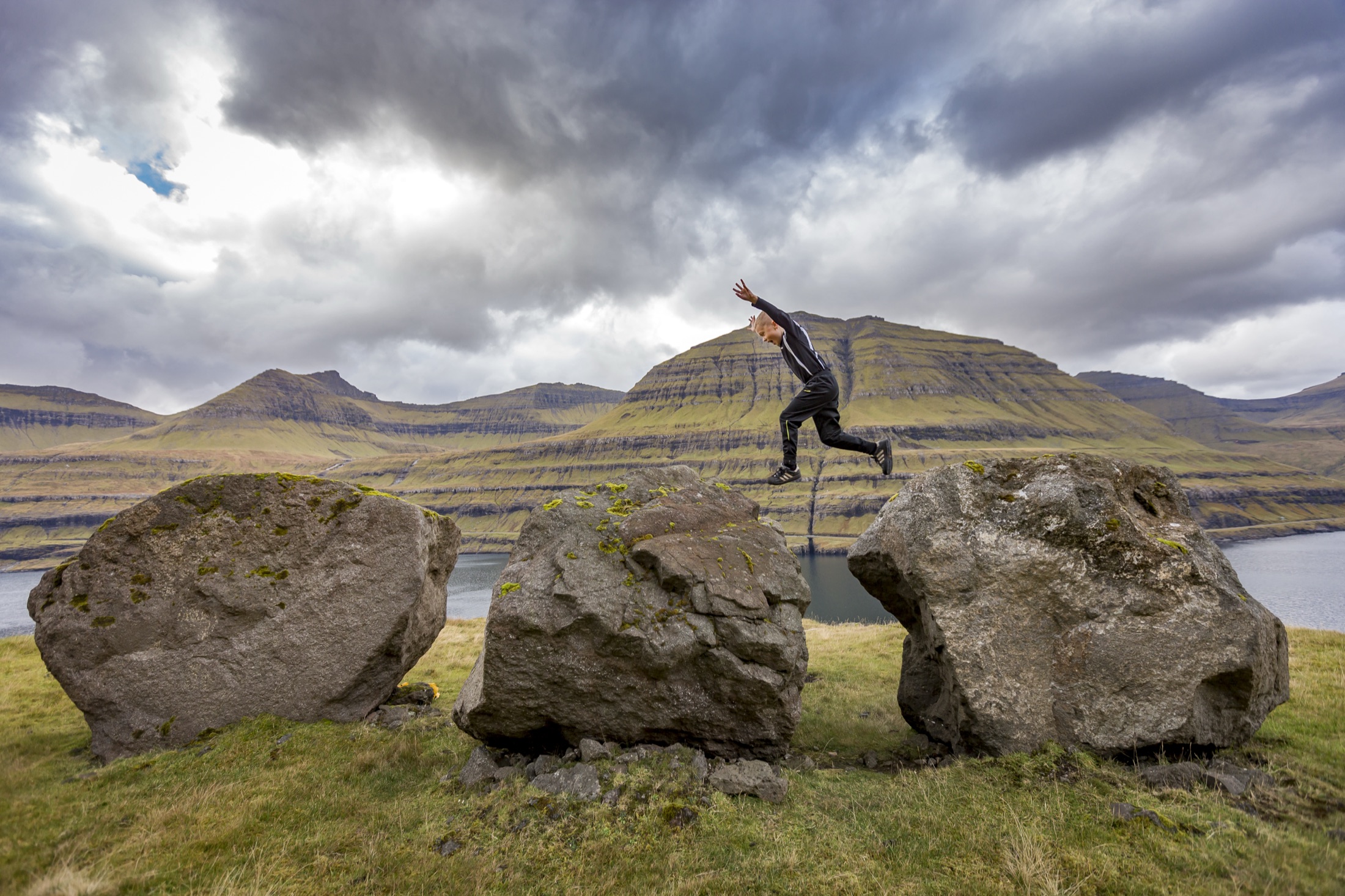 A child leaping between boulders above the fjord near Elduvík